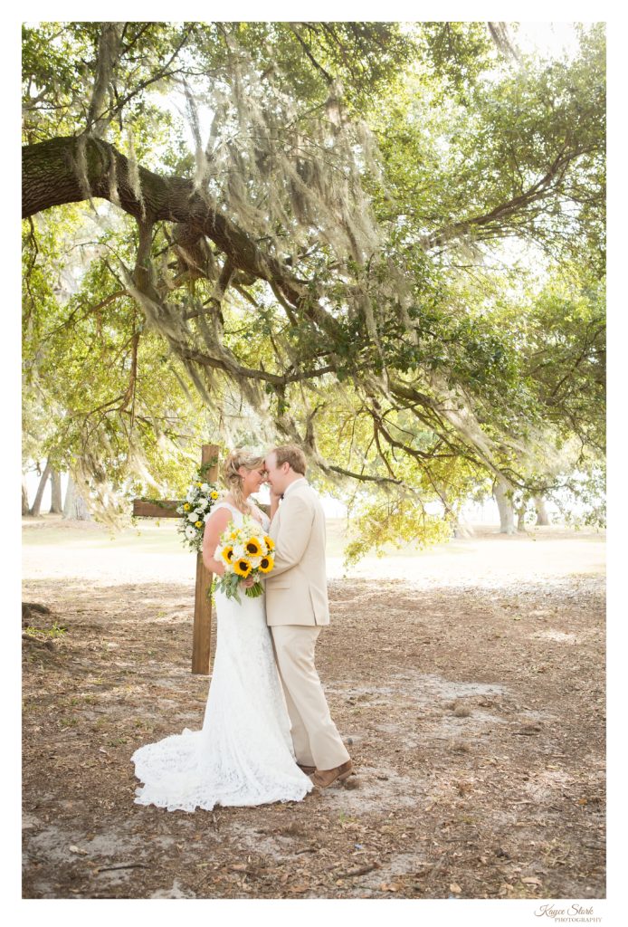 Bride and groom with sunflower bouquet under trees at beavoir for wedding