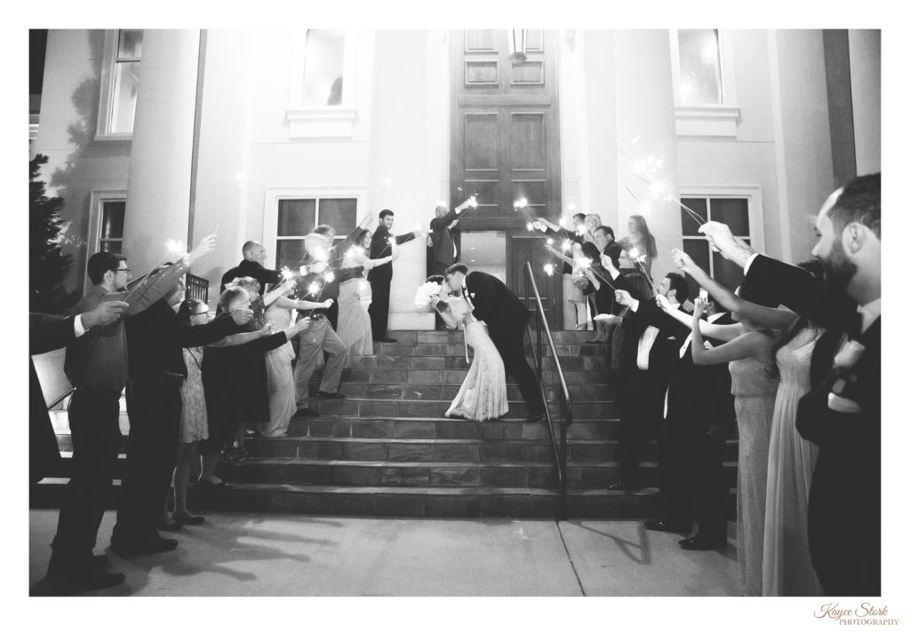 black and white photo of groom dip kissing bride on steps of the slavonian lodge in biloxi for grand sparkler exit during wedding reception