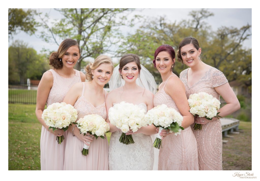 Bride in white lace overlay gown by eve of milady designer with bridesmaids in pink and gold dresses with white rose bouquets by pine hills floral