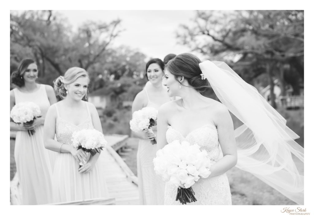 black and white photo of bride with cathedral veil looking back at bridesmaids while holding wedding bouquet