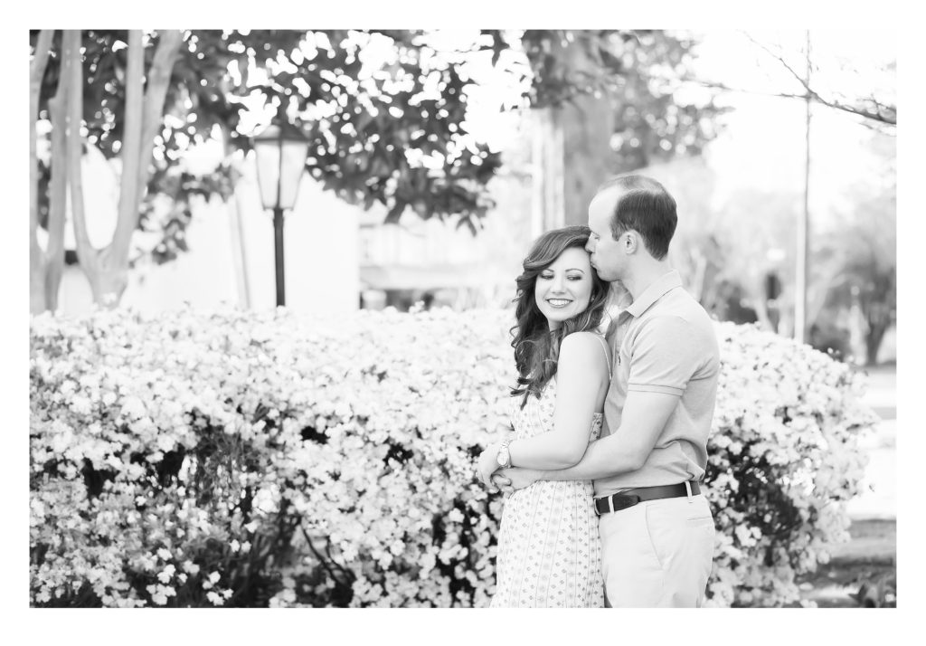 Black and white photo with groom sharing a kiss with his soon to be bride in khakis a polo and white dress at their engagement session in Tuscaloosa