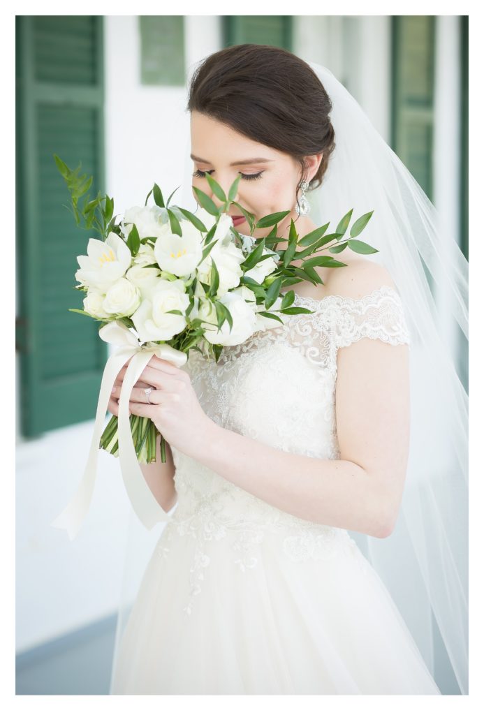 Bride wearing Sincerity Bridal holding bridal bouquet from After the Proposal close to face while pear engagement ring shows 