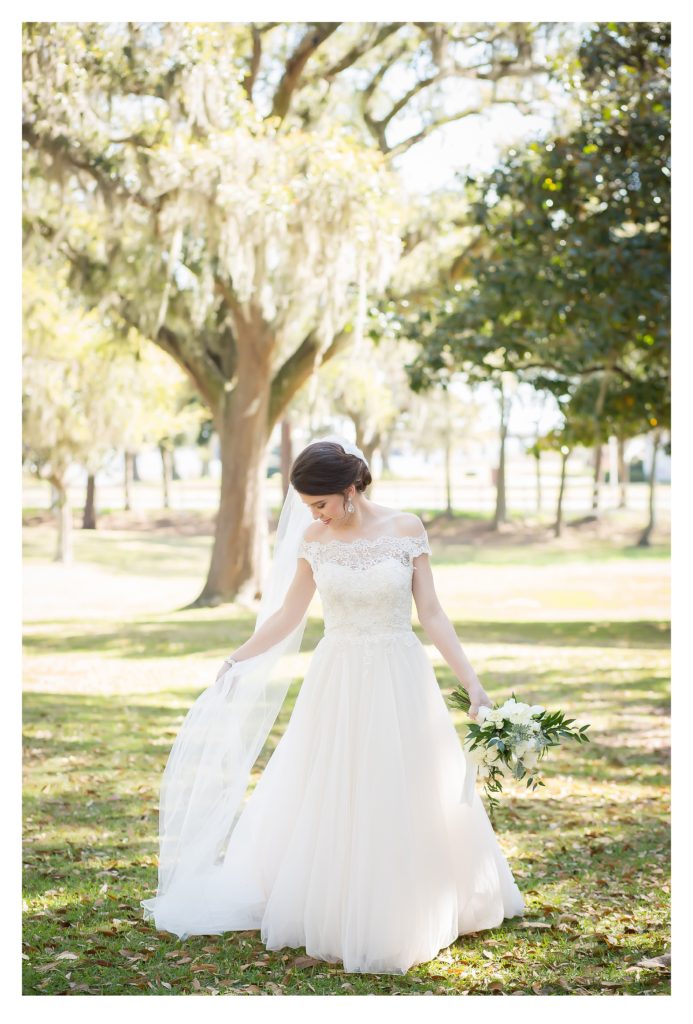Bride glancing at veil during bridal session with trees behind her at the old place wedding venue in gautier